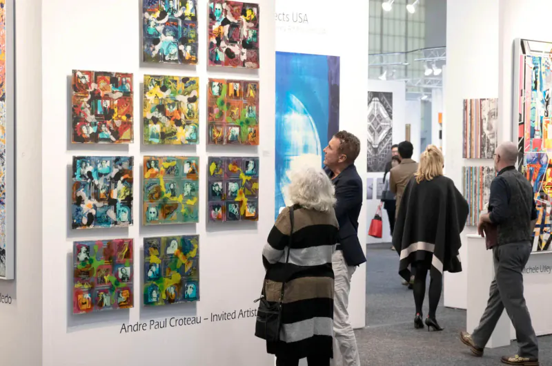 Visitors viewing André Paul Guillot's colorful abstract square paintings at ArtExpo Dallas gallery.