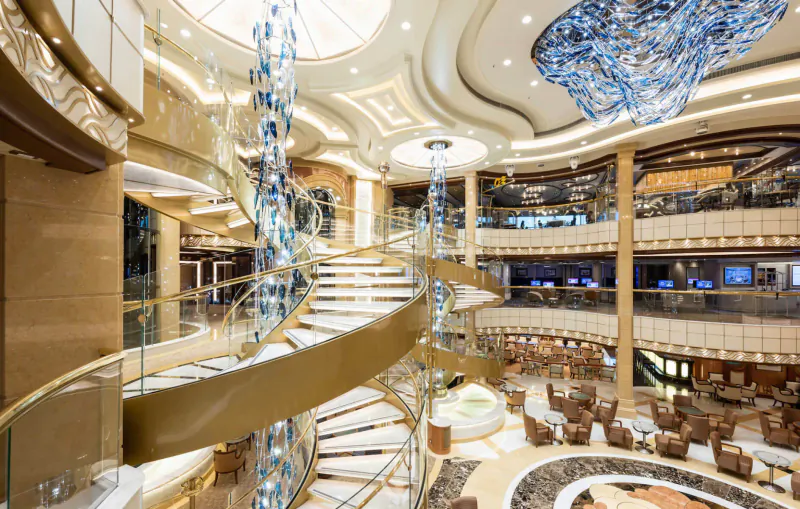 Grand multi-level atrium on Princess Cruises ship with curving golden staircase, blue chandelier, and lounge seating