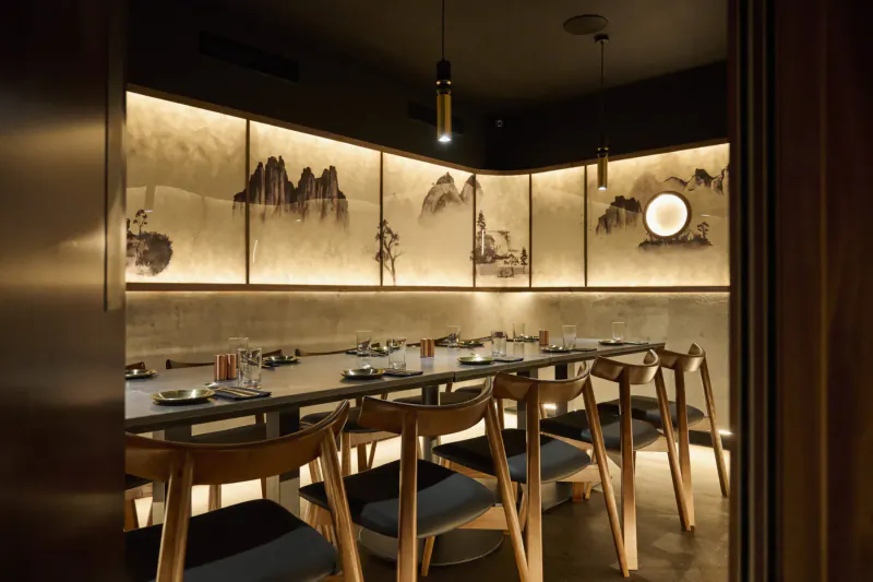 Elegant Korean restaurant interior with long wooden table, chairs, and illuminated ink mountain mural panels.