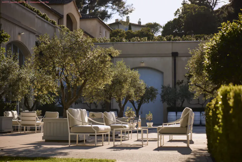 Elegant outdoor seating area with white chairs and tables amid olive trees at Léoube Estate courtyard, blue gate backdrop.