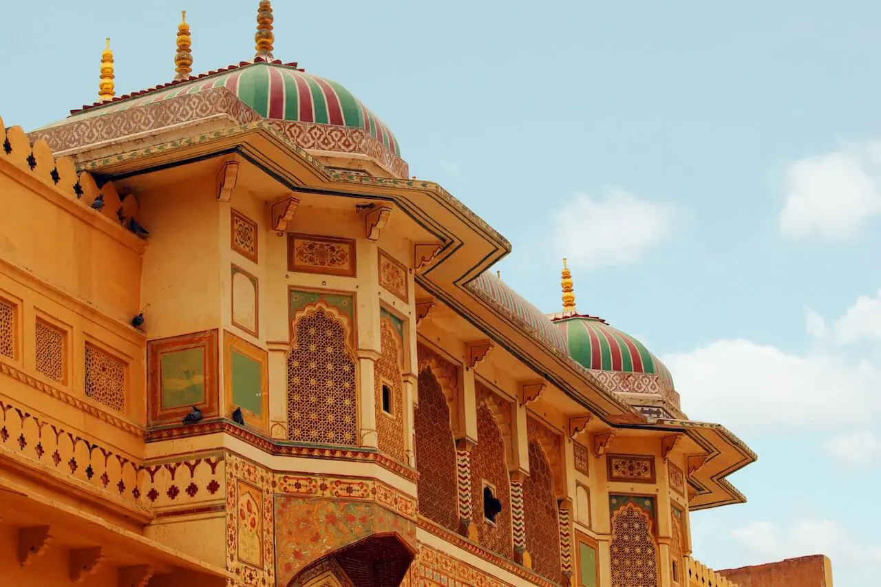 Ornate Rajasthani palace facade with yellow walls, green-red domes, intricate carvings, under blue sky