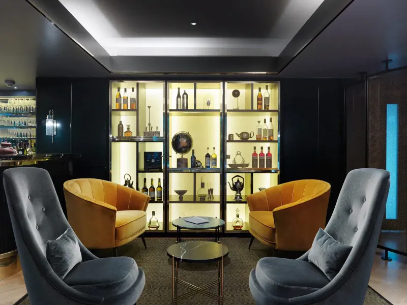 Elegant hotel lounge with illuminated liquor cabinet, velvet armchairs, and marble table at The Athenaeum, Mayfair.