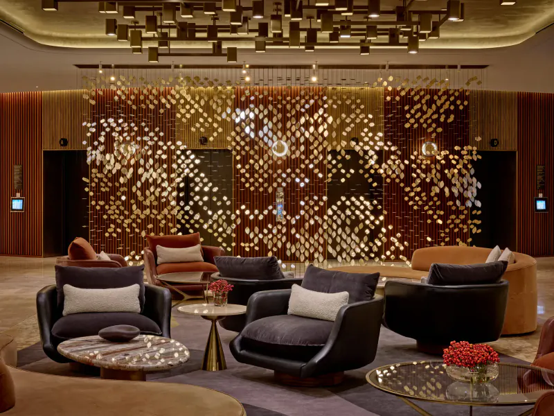 Park Corner Brasserie at London Hilton on Park Lane: luxurious lobby with gold geometric ceiling, illuminated wall panels, and plush armchairs around tables with flowers.