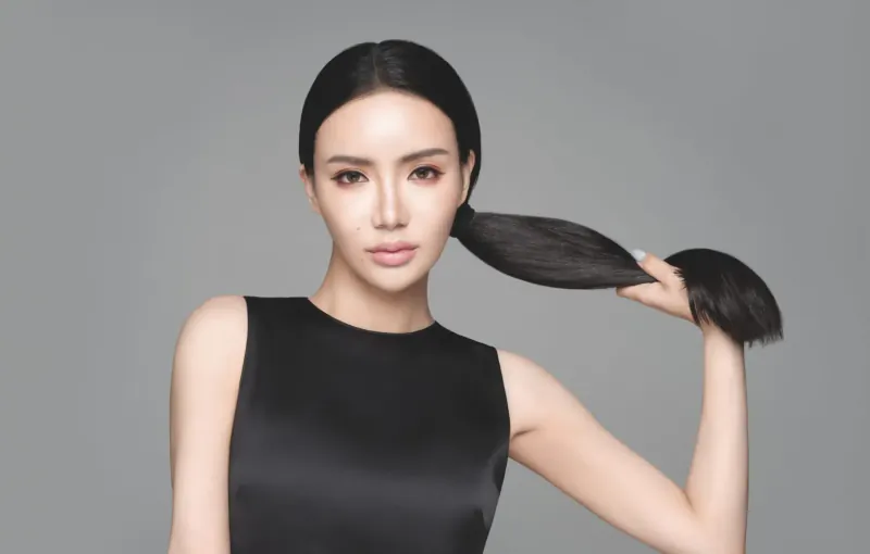 Emma Blunt with sleek ponytail held up, smiling in black sleeveless top against gray background