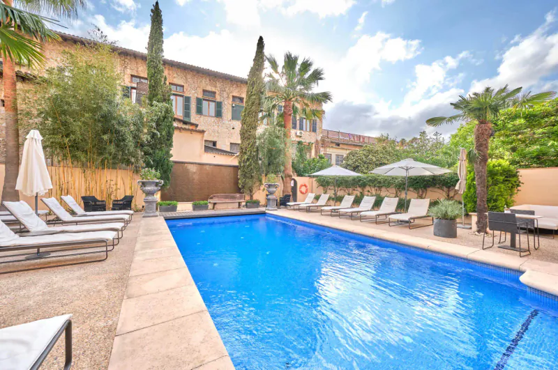 L’Avenida adults-only resort pool in Majorca: blue pool, lounge chairs, palms, stone villa under sunny sky