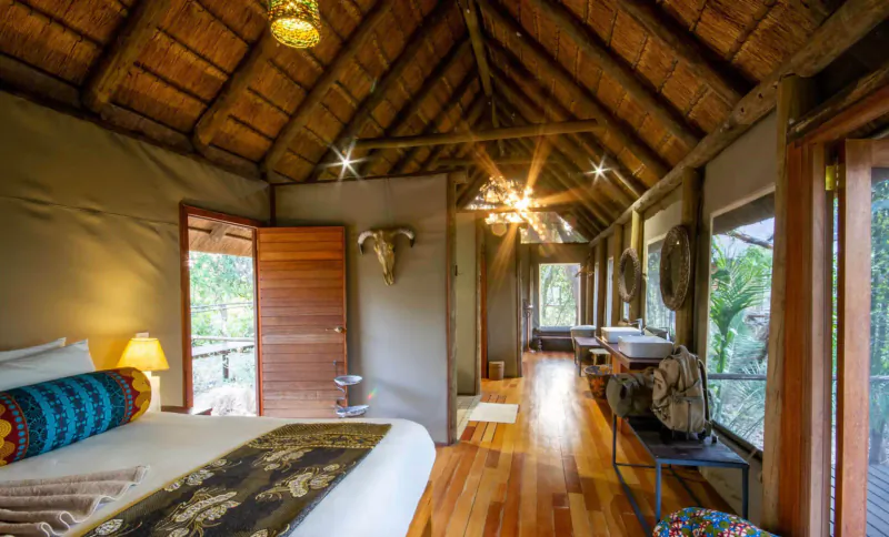 Luxurious safari tent bedroom in Botswana lodge with thatched roof, king bed, en-suite bathroom, and bush views.