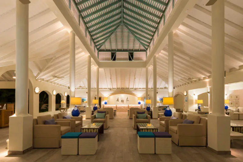 Elegant lobby at Blue Waters Resort & Spa Antigua with white columns, green ceiling, beige sofas, blue lamps, and wood floors.