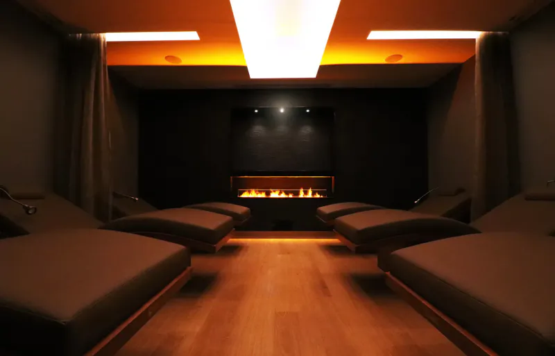 Luxurious spa lounge at Carden Park with reclining chairs, glowing fireplace, warm lighting, and wooden floor.