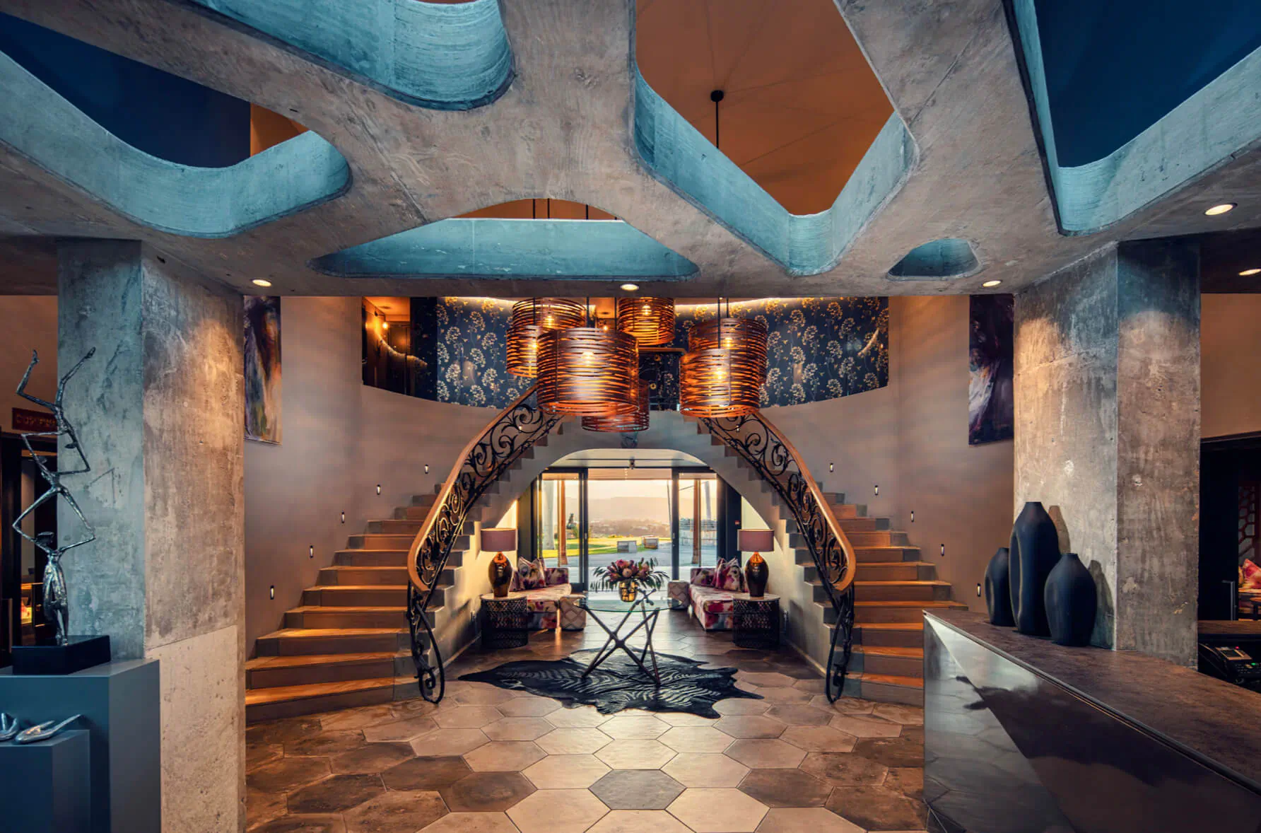 Sky Villa Boutique Hotel grand lobby with curved blue concrete ceiling, sweeping staircase, modern decor, and lounge seating.
