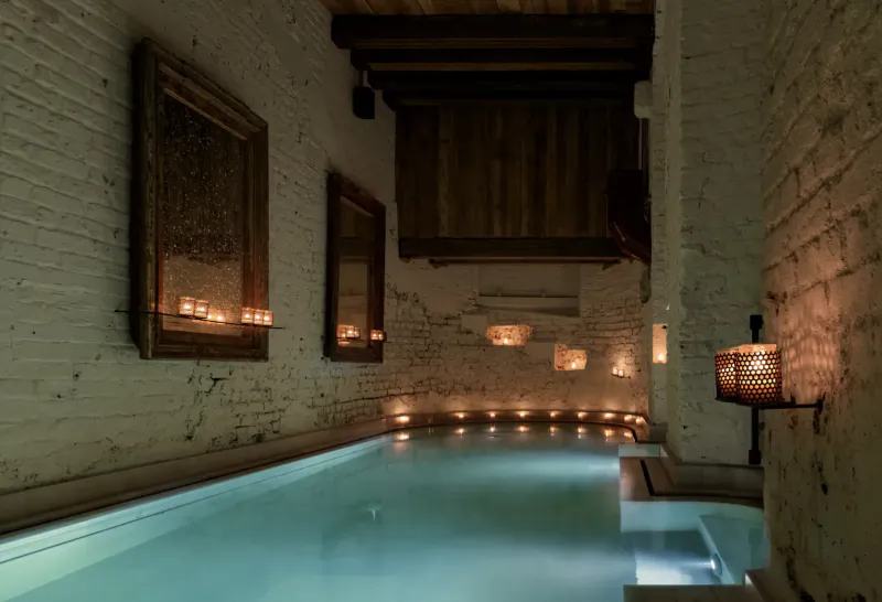 Candlelit indoor pool in white brick alleyway at Aire Spa, St. Martins Lane Hotel, with ornate framed mirrors.