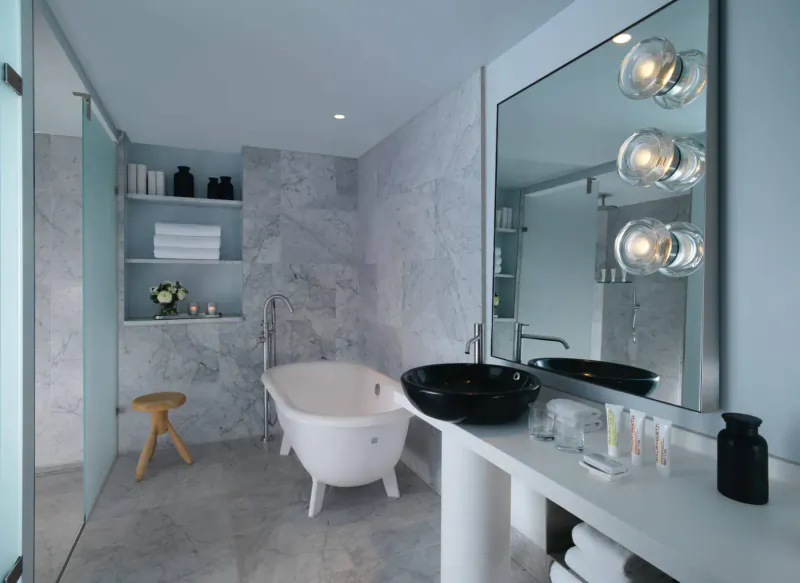 Elegant spa bathroom with white clawfoot bathtub, black sink, marble walls, towels, and modern lighting