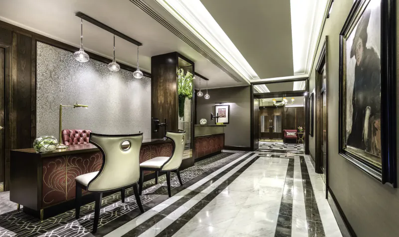 Elegant hotel reception desk with curved white chairs, floral arrangements, and artwork in luxurious Taj 51 Buckingham Gate lobby.