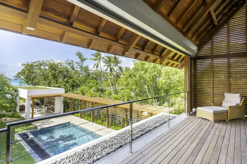 Aerial view of Villa Diamond's wooden balcony with lounge chair, infinity pool, tropical gardens, and ocean horizon in Mauritius.