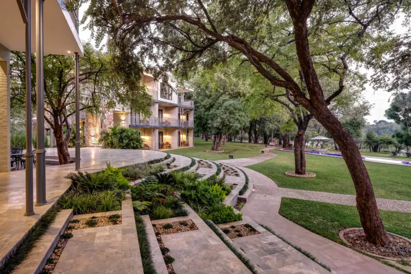 Palm River Hotel exterior near Victoria Falls: modern terraced gardens, winding paths, trees, and lawns.