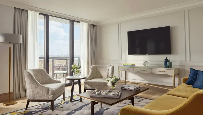 Elegant Carlton Tower Jumeirah hotel suite in London with yellow sofa, armchairs, coffee table, TV, and city view balcony.
