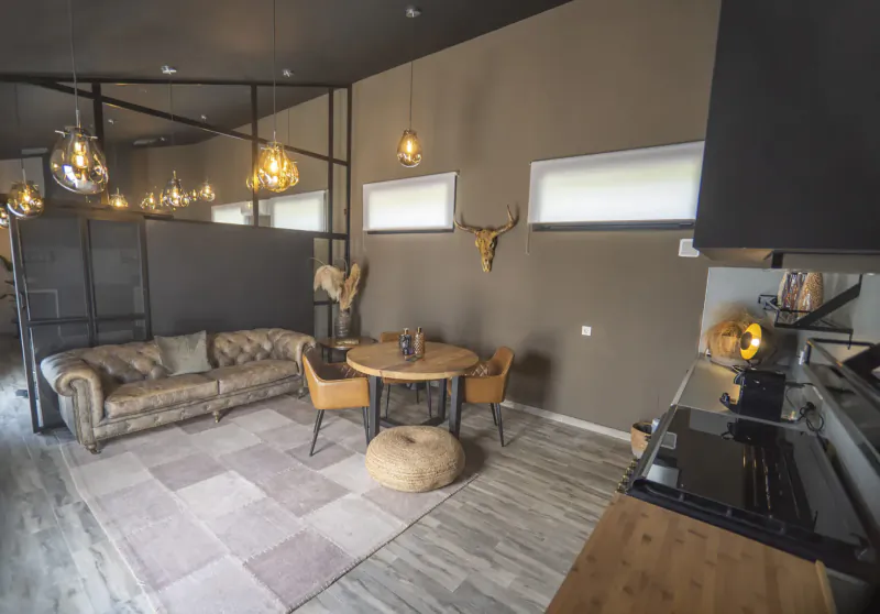 Modern lounge in La Vuelta Boutique Hotel with tufted sofa, round table, chairs, pouf, cow skull, pendant lights, and kitchenette.