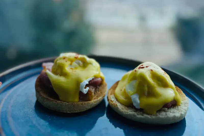 Two poached eggs with hollandaise and ham on English muffins on a blue plate at Delta Hotel Swansea.