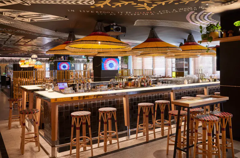 Stylish Mama Shelter bar in East London with wooden stools, colorful pendant lights, plants, and eclectic decor.