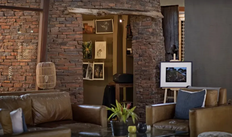 Cozy lounge in Marataba Game Lodge with leather armchairs, plants, art on brick walls, and arched doorway.
