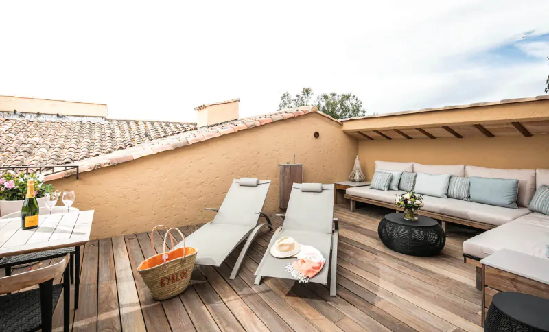 Luxury rooftop terrace at Byblos Palace hotel in Saint-Tropez with lounge chairs, champagne, plates, and plants on wooden deck.
