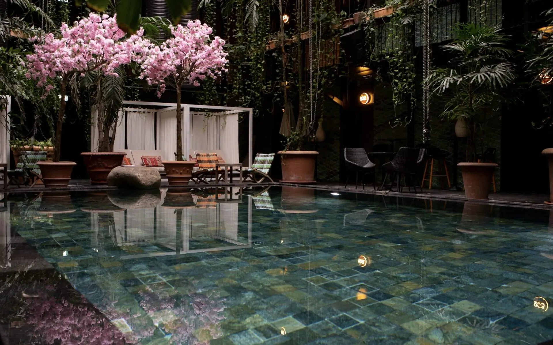 Tranquil tropical pool oasis at Manon Les Suites with pink cherry blossoms, palms, loungers, and green-tiled water.