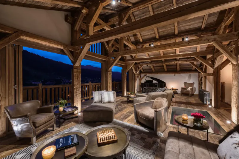 Luxurious mountainside chalet living room with wooden beams, plush seating, grand piano, and alpine night views.