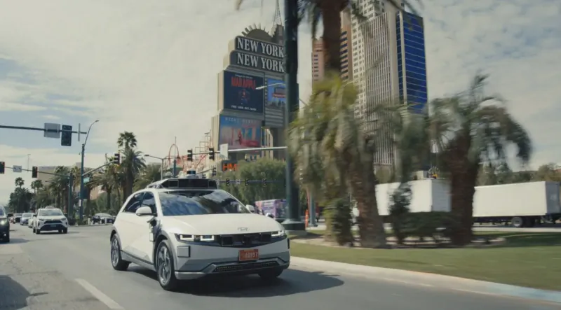 White Hyundai IONIQ 5 robotaxi with lidar drives past 'Welcome to Fabulous Las Vegas' sign and palms on Vegas street.
