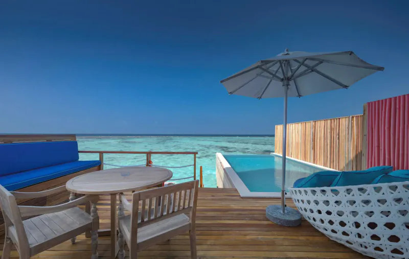Luxury overwater villa in Maldives with private infinity pool, wooden deck, table, chairs, umbrella, and ocean view
