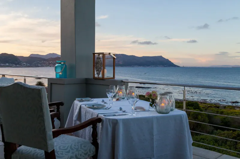 Romantic candlelit dinner table on balcony at Tintswalo Boulders, overlooking ocean and mountains at sunset