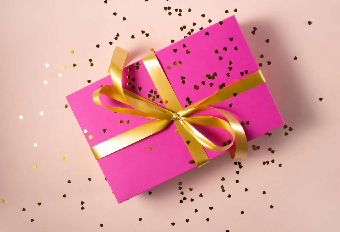Pink gift box with gold ribbon bow on pink background scattered with gold stars