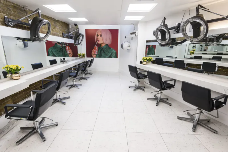 Modern Neville Hair and Beauty salon interior with rows of black salon chairs, hairdryers, and large portrait of woman in green.