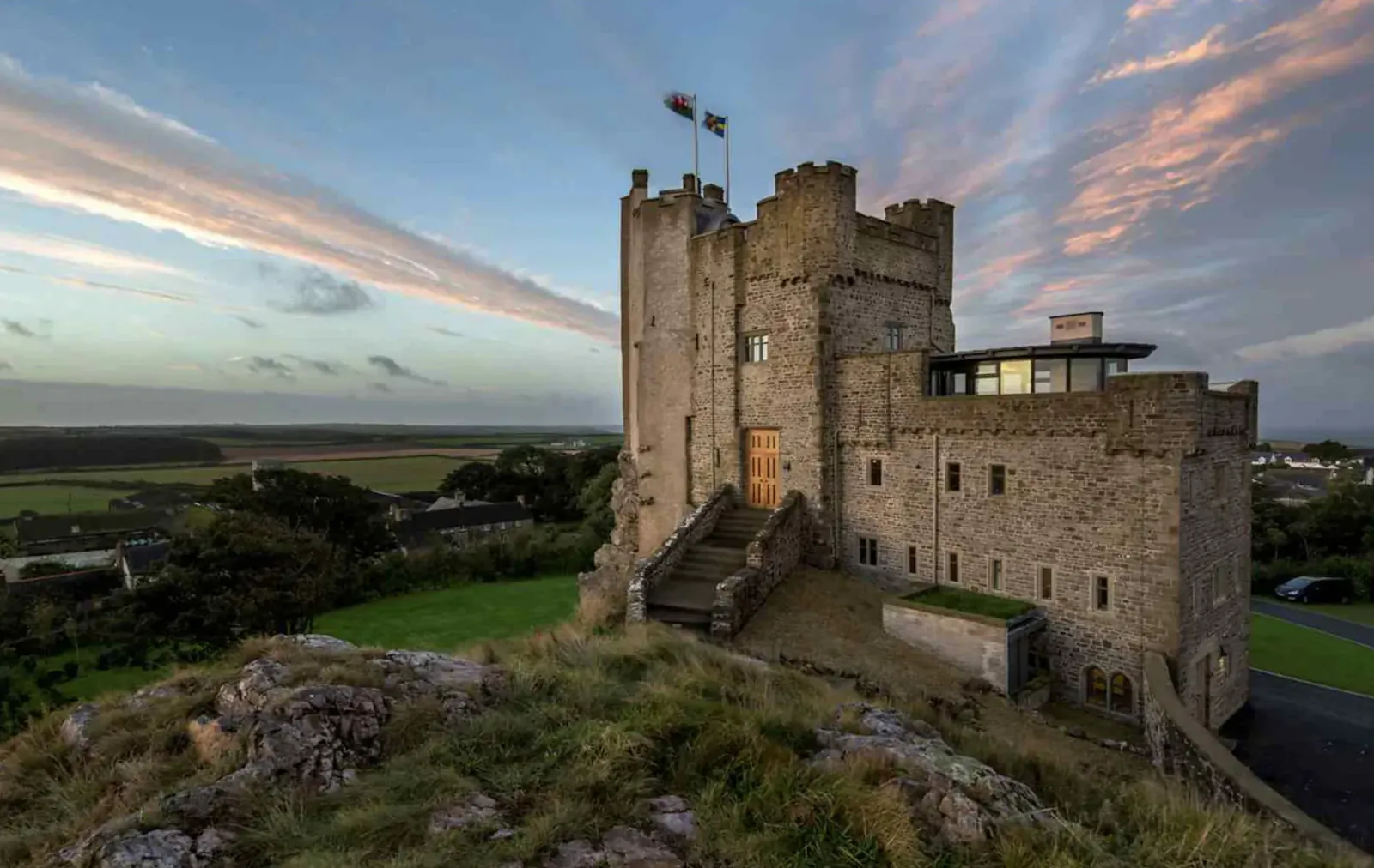 Roch Castle on grassy hilltop at sunset, with 360-degree Pembrokeshire views, stone towers and flags flying.