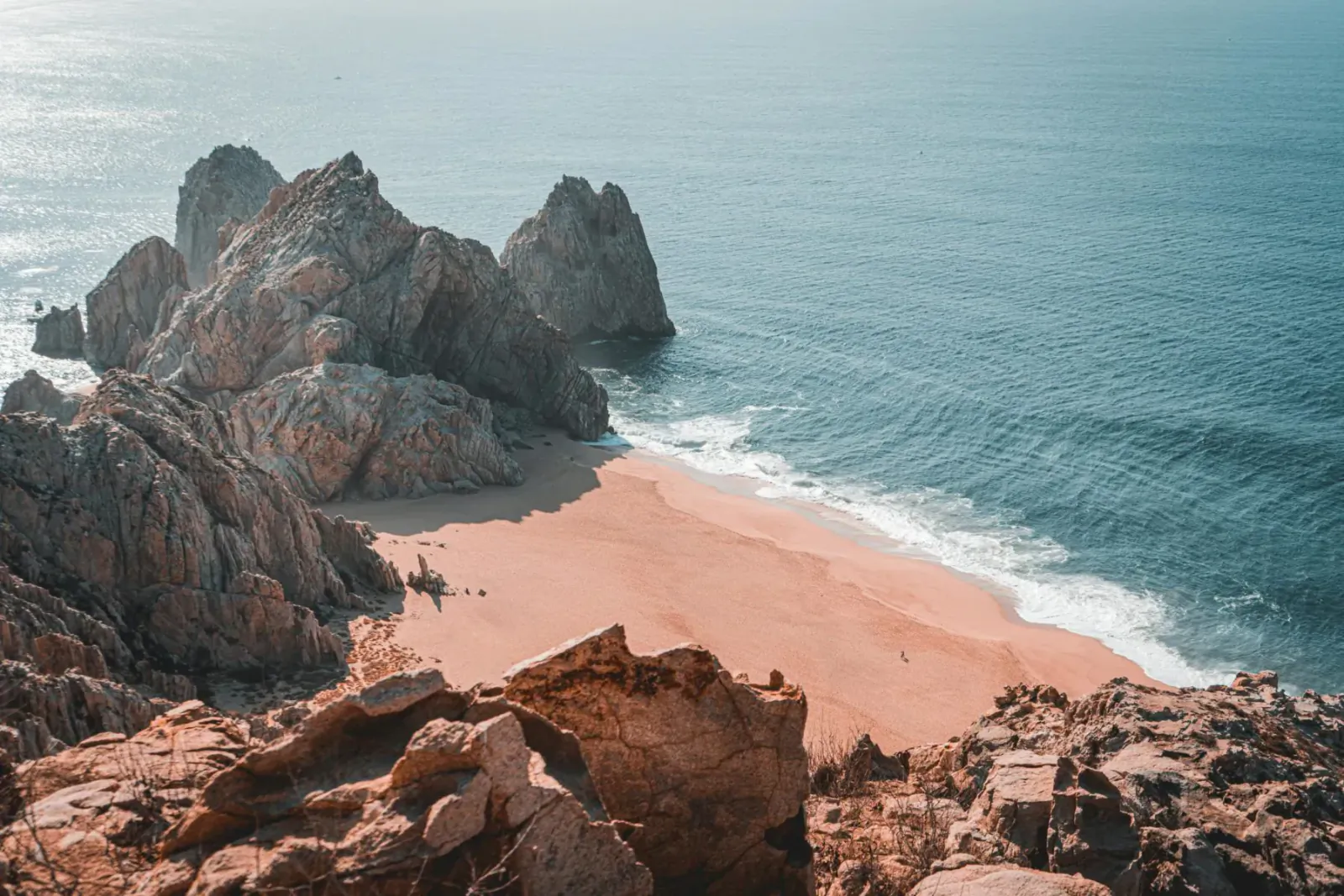 Aerial view of rugged rocky cliffs framing a sandy beach meeting turquoise ocean waves in Mexico.