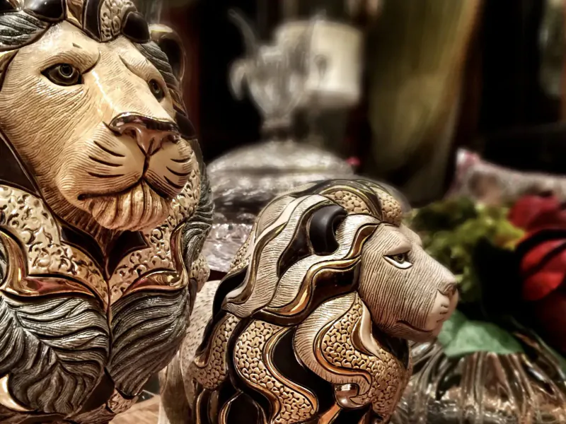 Two ornate carved lion sculptures side by side in a gallery display with metallic and floral accents