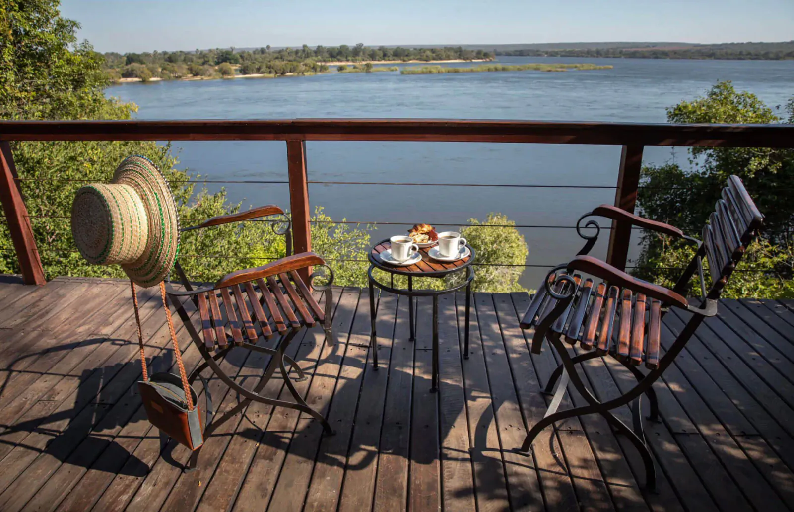 Wooden deck overlooking lake with two wicker chairs, small table with teacups, and straw hat at The River Club oasis.