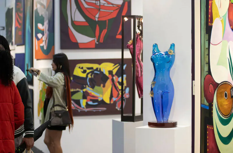 Woman points at blue female sculpture amid colorful abstract paintings at Artexpo Dallas gallery