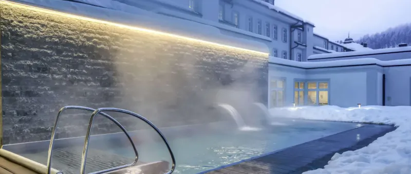 Steaming hot tub with ladders in snowy courtyard at Grand Hotel Des Bains Kempinski St. Moritz, alpine winter setting.