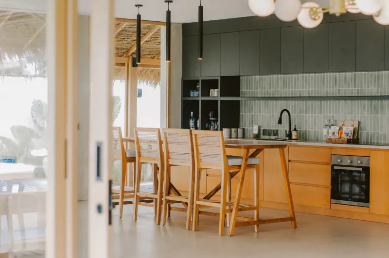 Modern kitchen in beachfront villa with wooden bar stools, open doors to pool and ocean view.