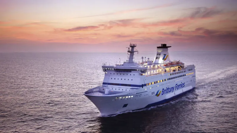 White Brittany Ferries ship sailing on sea at sunset, heading to Saint-Malo, France.