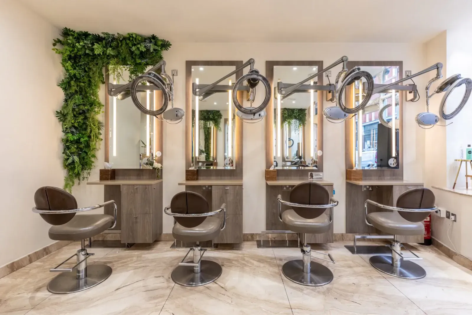 Modern MichaelJohn salon interior with four styling stations, swivel chairs, mirrors, dryers, and green wall plants.