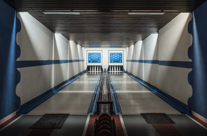 Bowling alley with blue-lit lanes, two glowing score screens, and centered pins at the end.