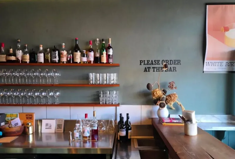 Bar counter with liquor bottles, glassware, dried flowers, and sign: 'Please order at the bar'