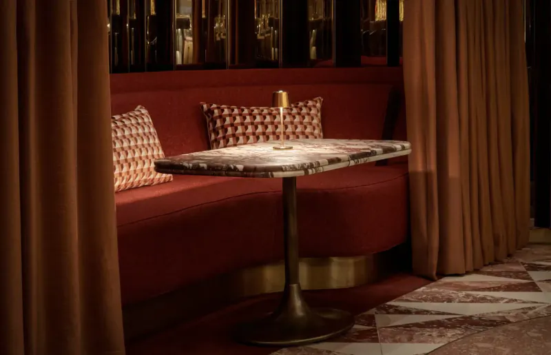 Cozy red velvet booth with patterned pillows, marble table, lit candle at Revery Bar’s afternoon tea gallery
