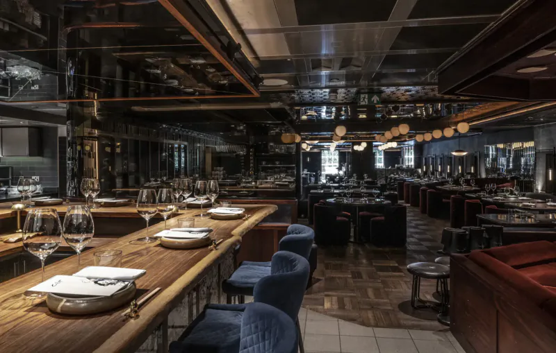 Elegant Lucky Cat Mayfair restaurant interior with wooden bar, blue velvet stools, set tables, and warm pendant lights.