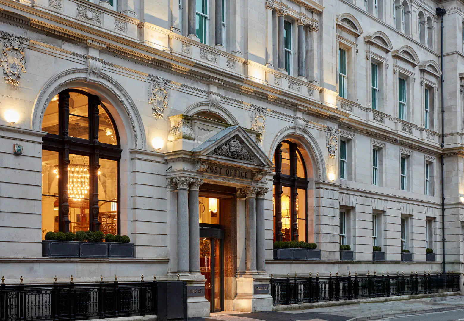 Elegant 'ME London' hotel entrance at night with illuminated arched windows, chandeliers, and planters.