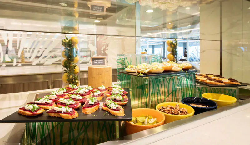Elegant cruise buffet display with bruschetta on black platters, buns, salads in yellow bowls, and lemon garnishes.