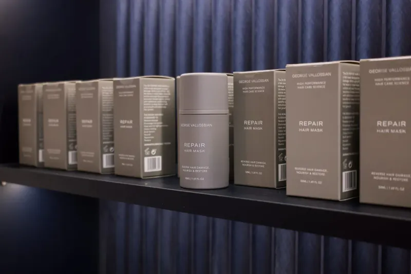 Shelf of gray 'Hair Repair' product boxes and bottles in a salon against blue curtain backdrop.