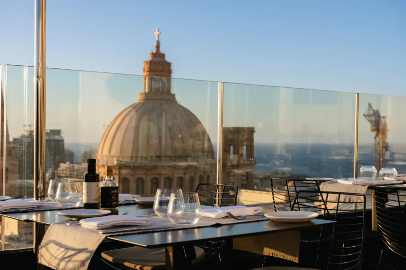 Rooftop table with wine overlooking Valletta's domes and historic skyline at sunset, Embassy Valletta Hotel.
