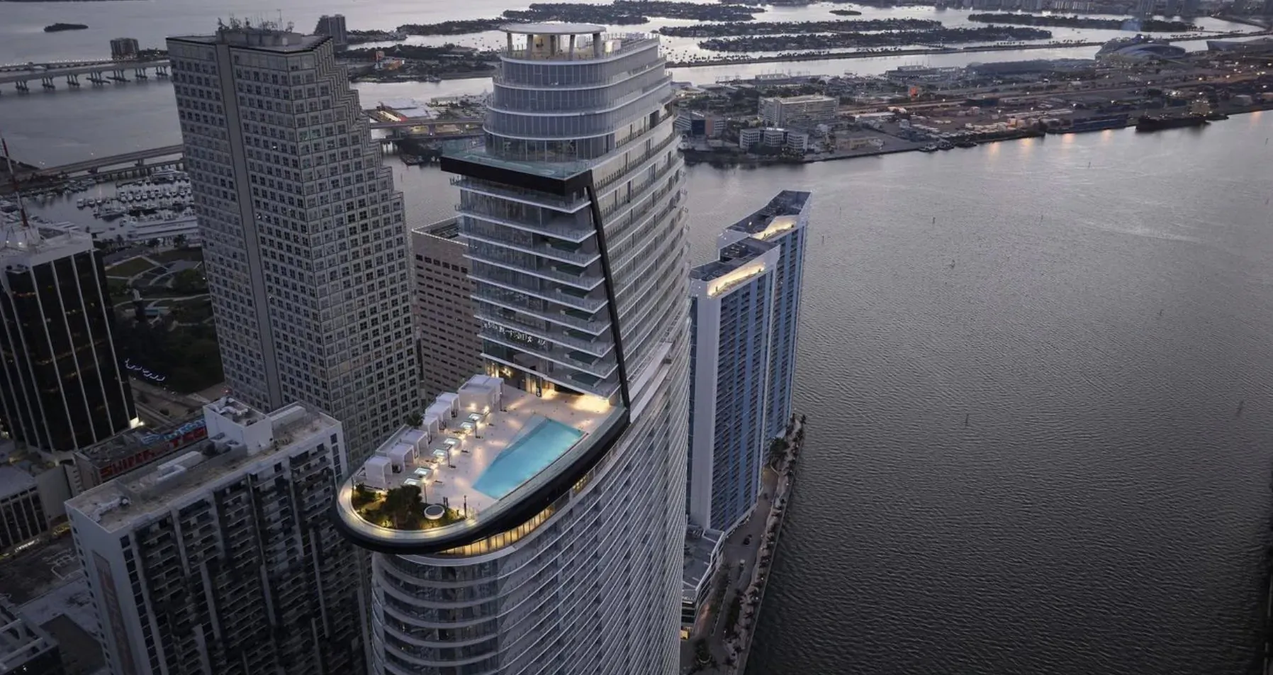 Aerial view of Aston Martin Residences Miami: sleek high-rise with rooftop infinity pool overlooking city skyline and bay