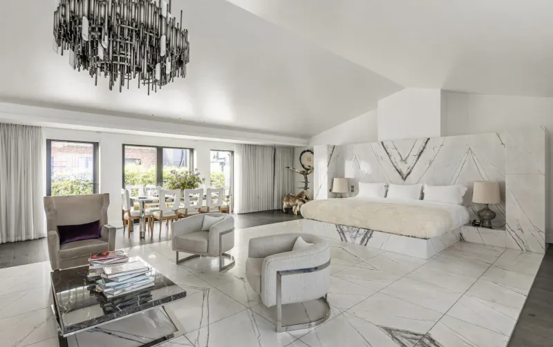 Luxurious white bedroom suite at The Mandrake with chandelier, king bed, dining table, and modern art decor.